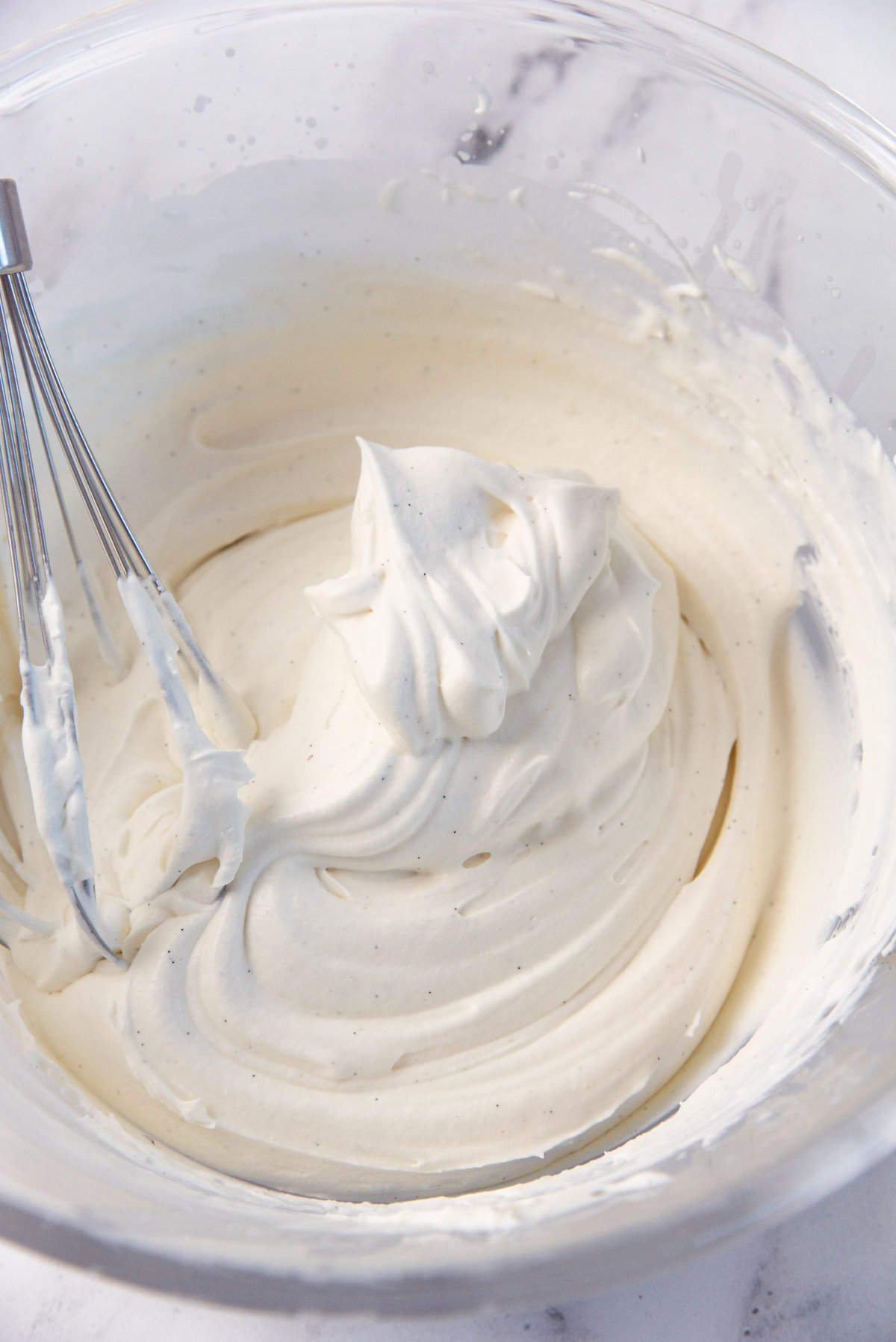 A close up image of heavy cream that has whipped for the pavlova topping, showing stiff peaks, a smooth texture and vanilla bean seeds flecked throughout.
