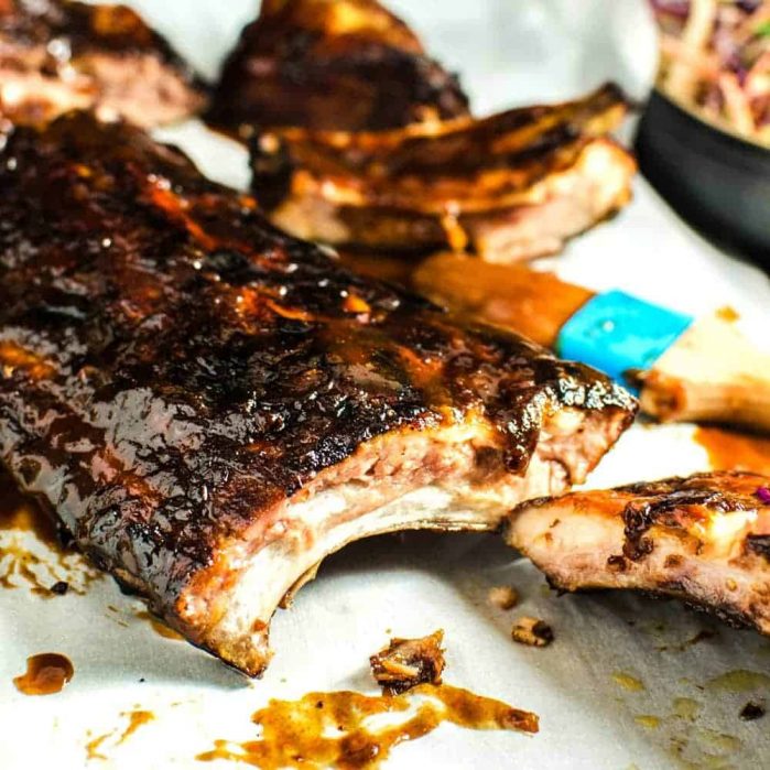 Baby back ribs brushed with habanero peach BBQ sauce and a brush next to it.