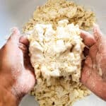 Two hands holding a clump of dough that has been squeezed together to check the consistency of the dough.