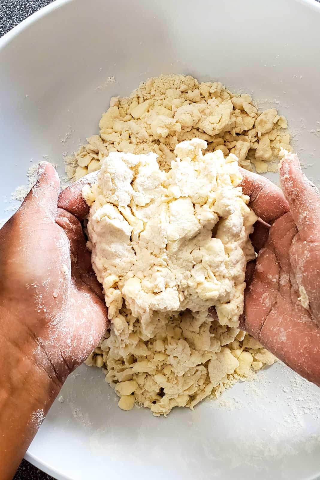 Two hands holding a clump of dough that has been squeezed together to check the consistency of the dough.
