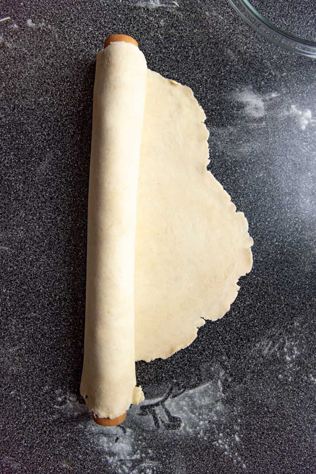 Rolled out pie dough, being rolled onto a rolling pin so that it's easier to transfer.