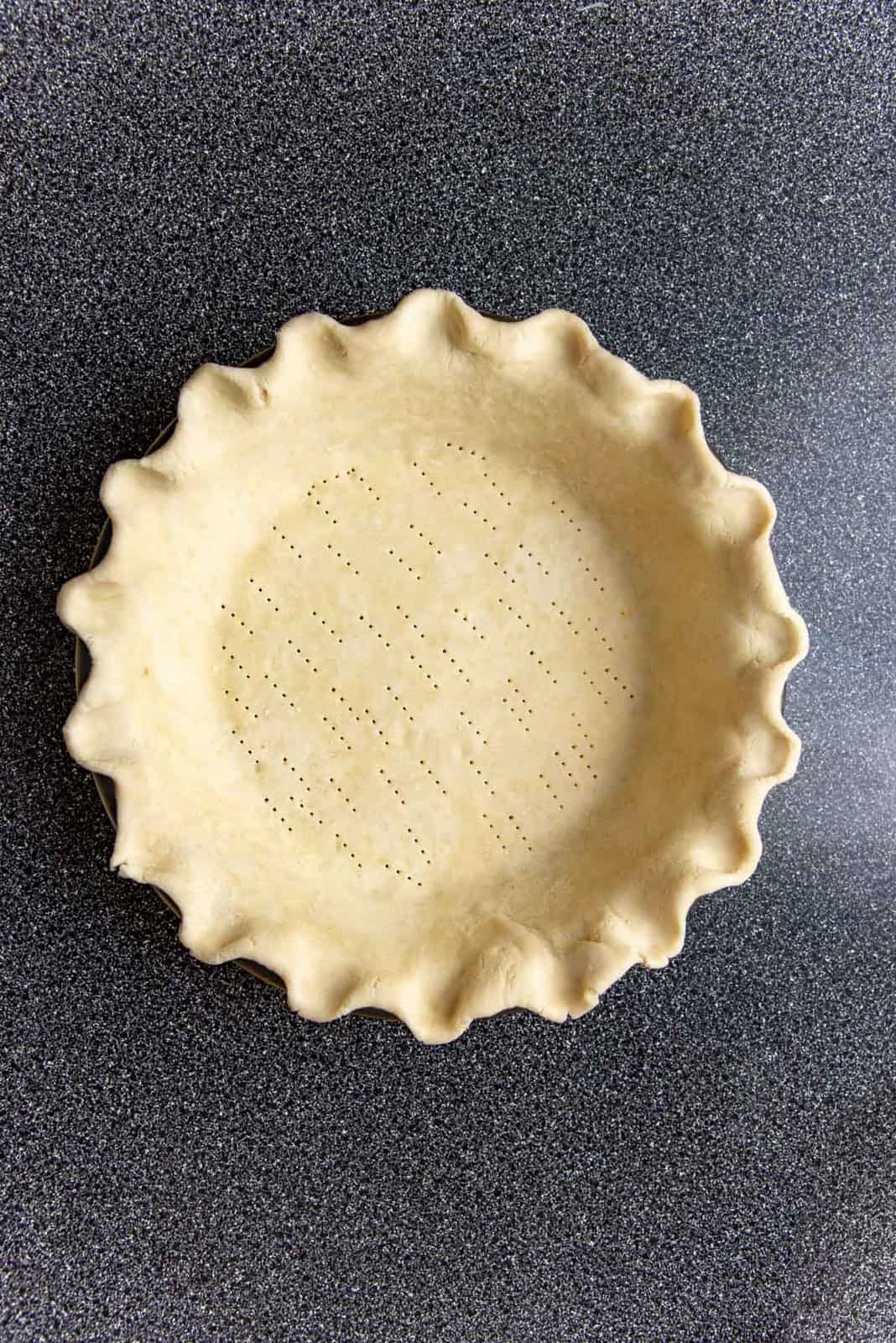 An overhead view of the chilled pie crust with fluted edges and the base pricked with a fork.