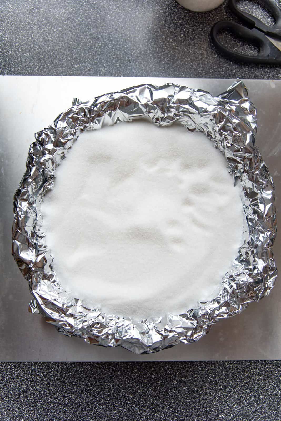 The foil lined pie plate filled with sugar prepared for blind baking,