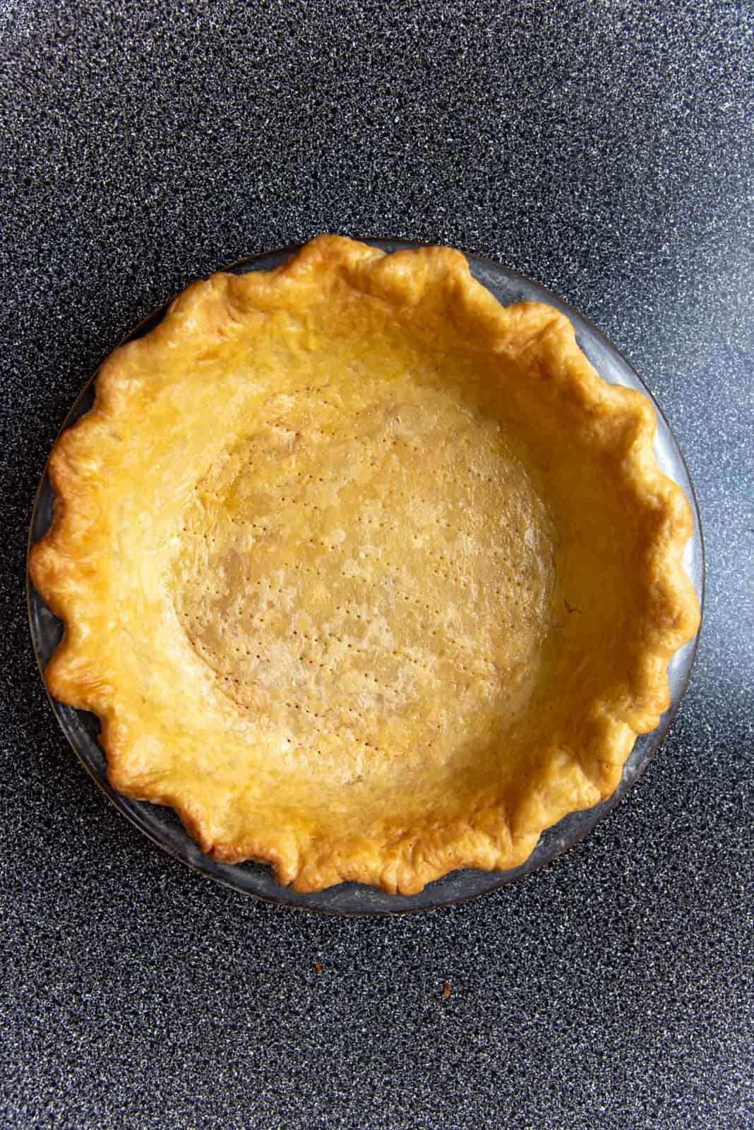 A fully baked pie crust placed on a dark background.
