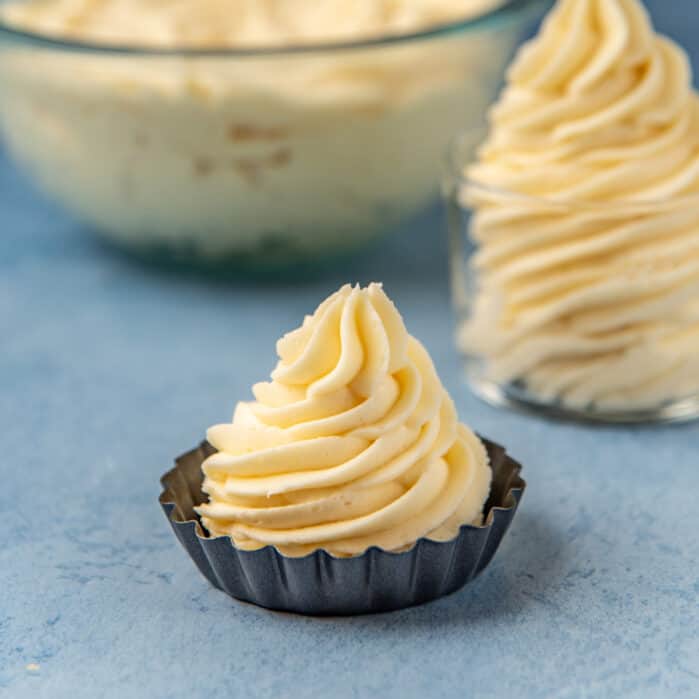 Cream cheese frosting piped onto a small baking mold on a blue work surface.