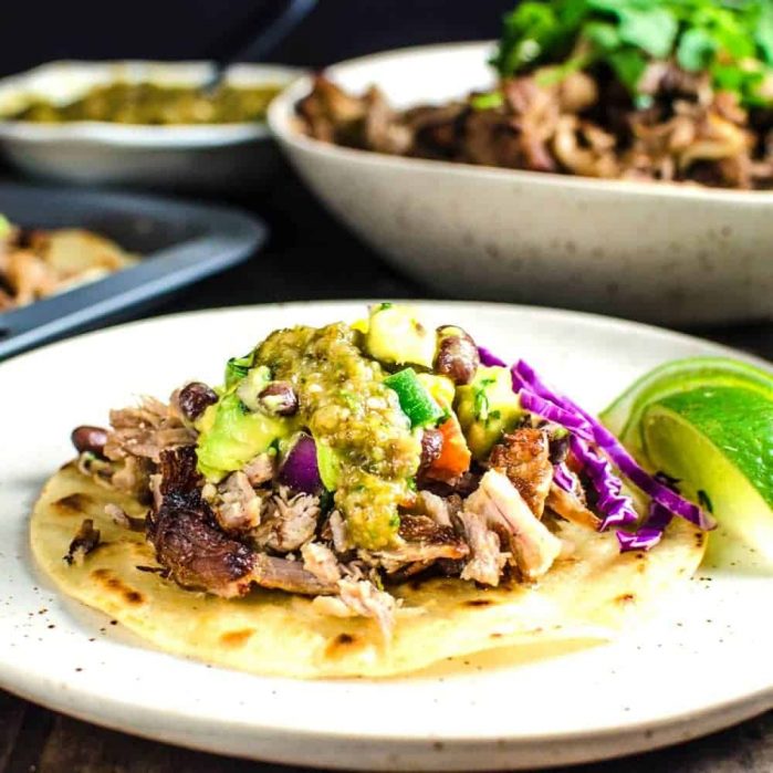 Toasted tortilla on a white plate topped with pork carnitas, mango black bean salsa and salsa verde.