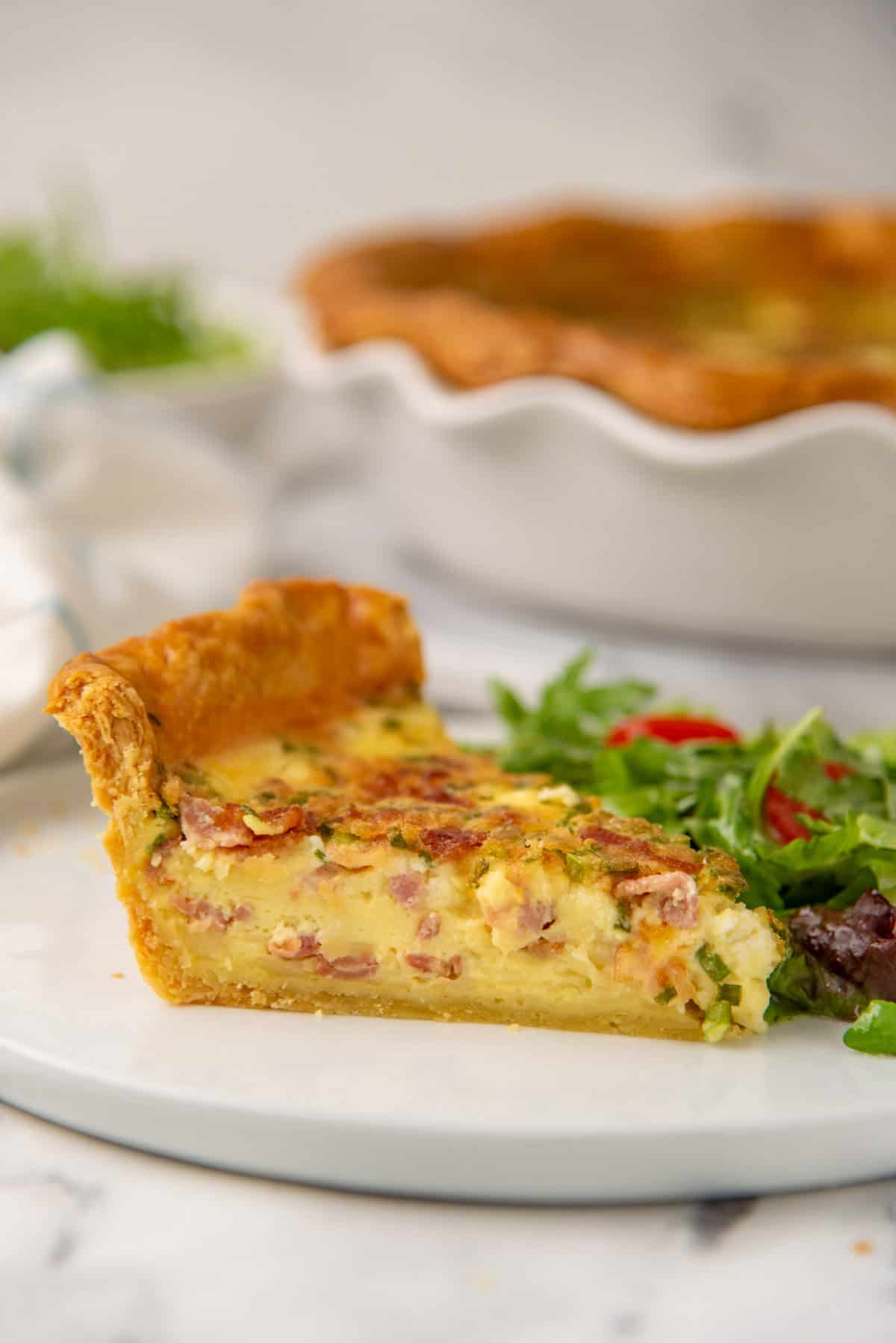 A close up of the quiche lorraine slice on a plate, showing the crust and filling cross section.