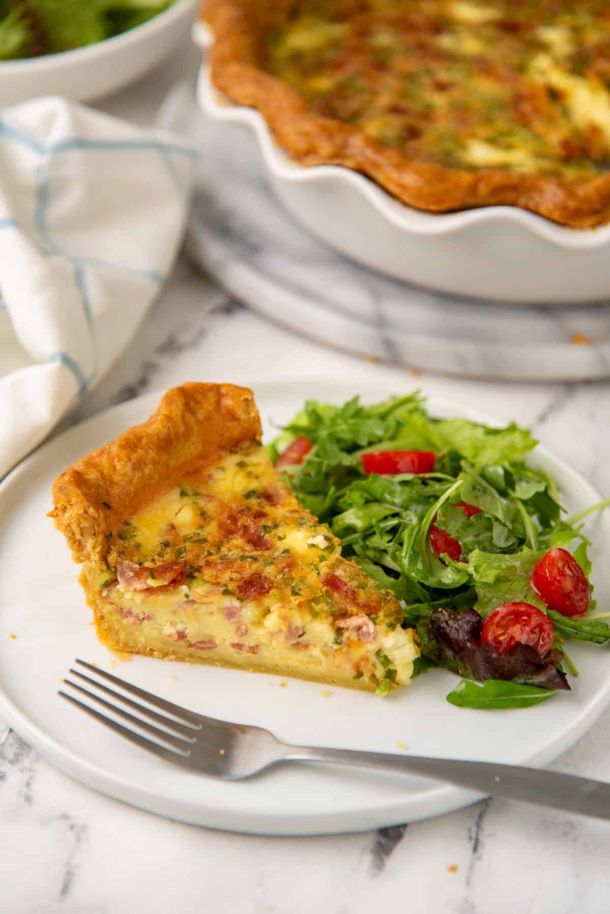 Slice of lorraine quiche served on a white plate with a side salad.