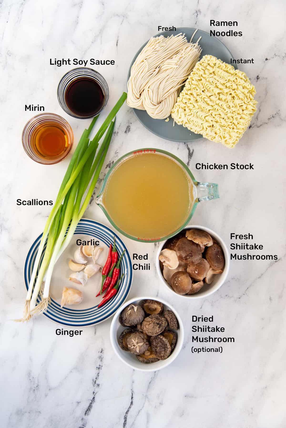 Simple and easy Shoyu Ramen broth ingredients on a marbled counter. Clockwise from top, Fresh and Instant ramen on a blue plate, Chicken stock, fresh shiitake, dried shiitake (optional), red chili, ginger, garlic, scallions, mirin and light soy sauce.