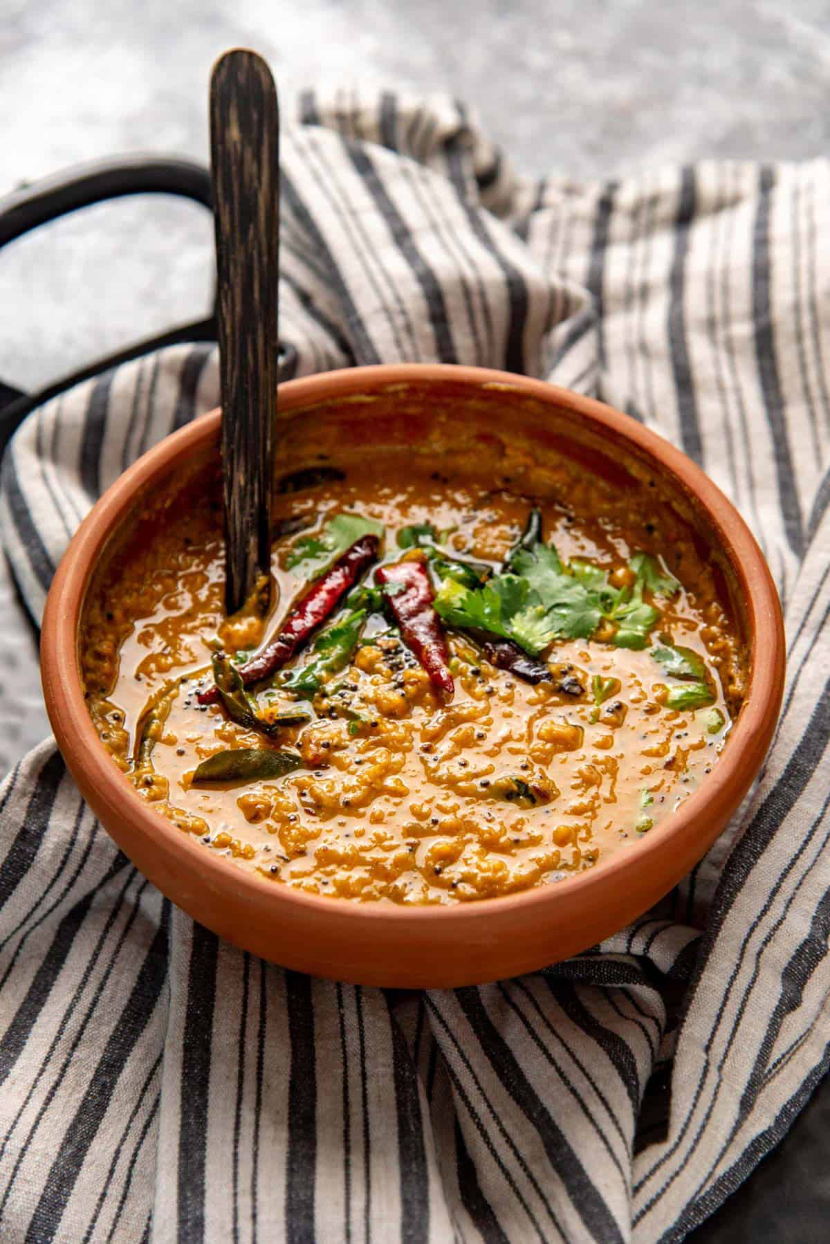 Dal curry with coconut milk served in a clay pot with a wooden spoon.