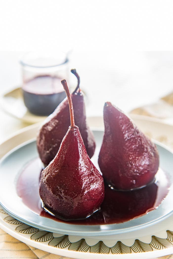 three red wine poached pears on a blue plate with red wine syrup, with extra red wine syrup in the background. 
