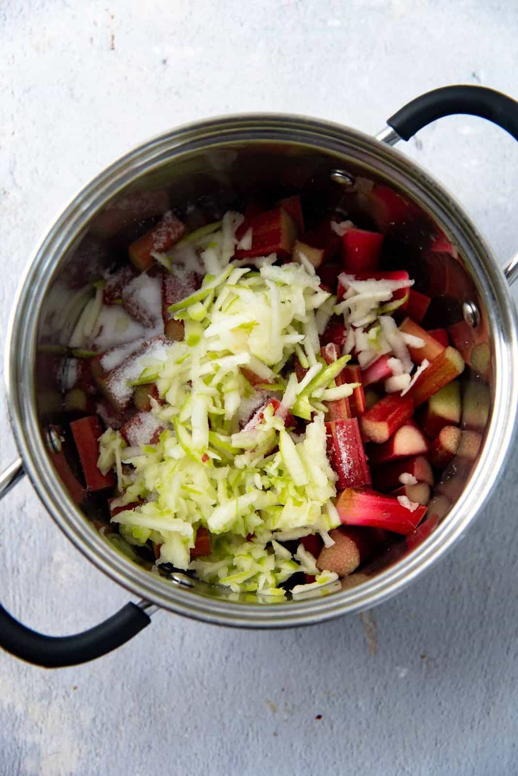 Adding apple to the rhubarb in a pot.