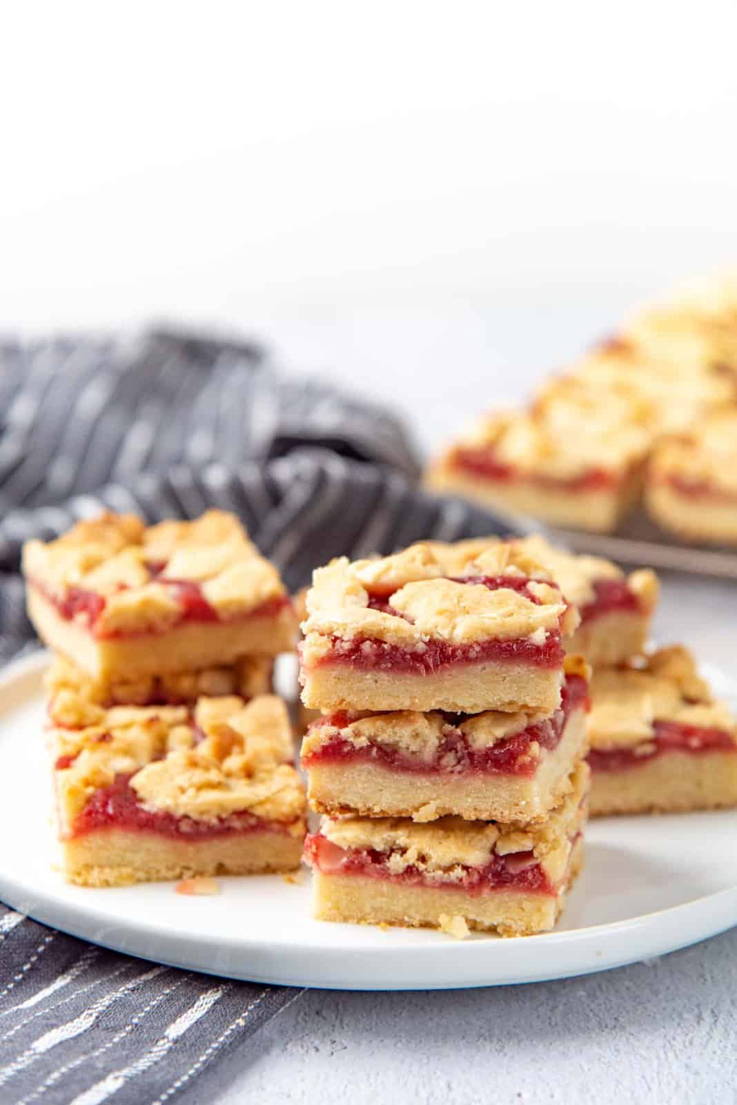Three rhubarb crumble slices stacked on a white plate.
