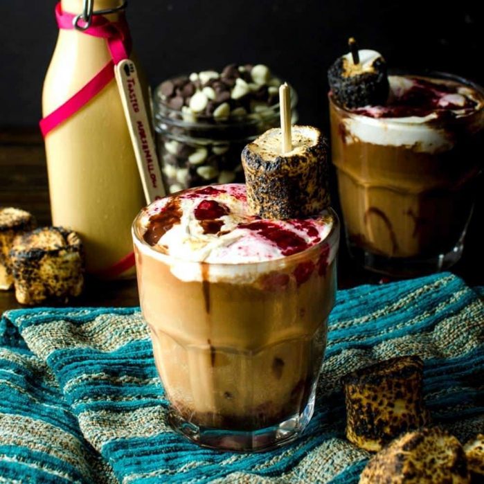Rocky road hot chocolate in a glass, served with raspberry jam and a toasted marshmallow on top.