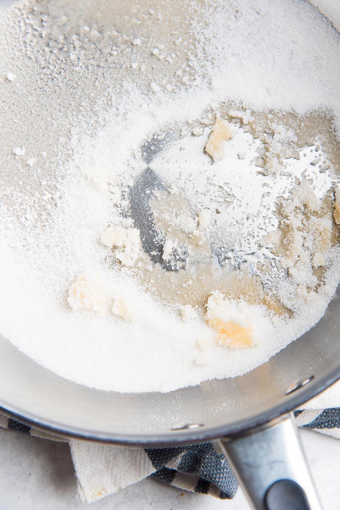 White sugar sprinkled on the bottom of a pan, half way through making a dry caramel for salted caramel pastry cream.
