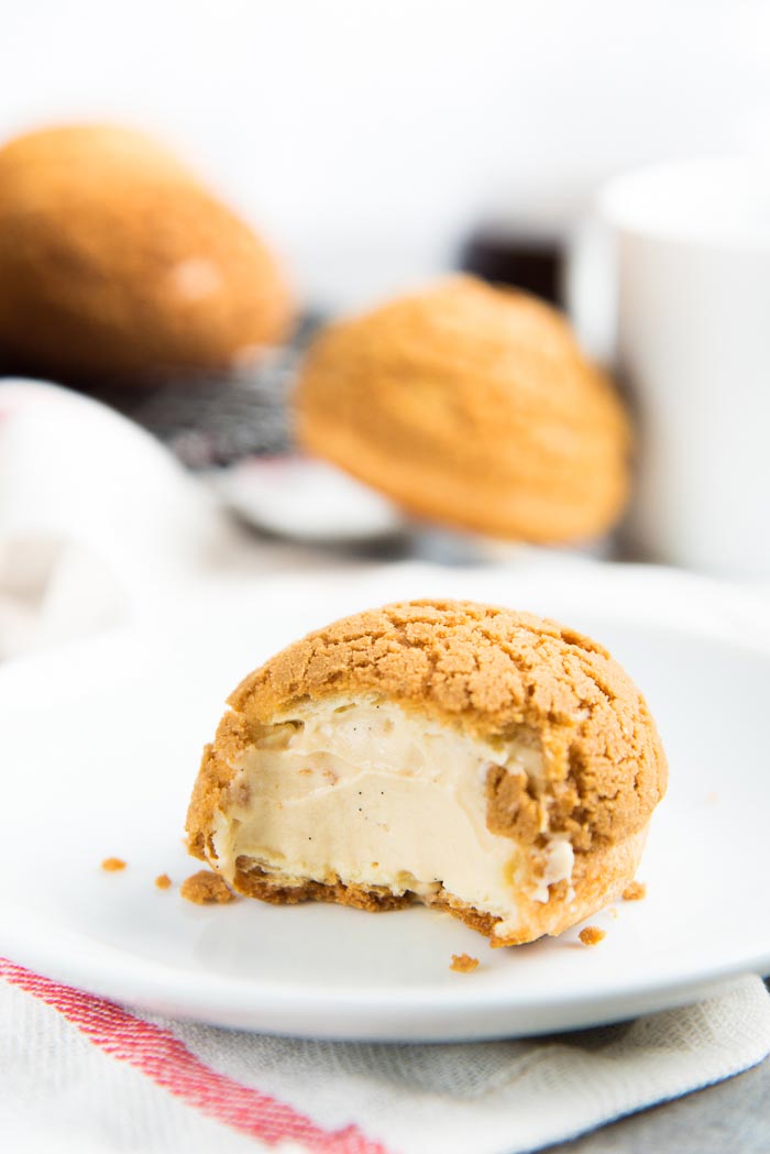 A half eaten choux au craquelin with salted caramel cream filling on a white plate.