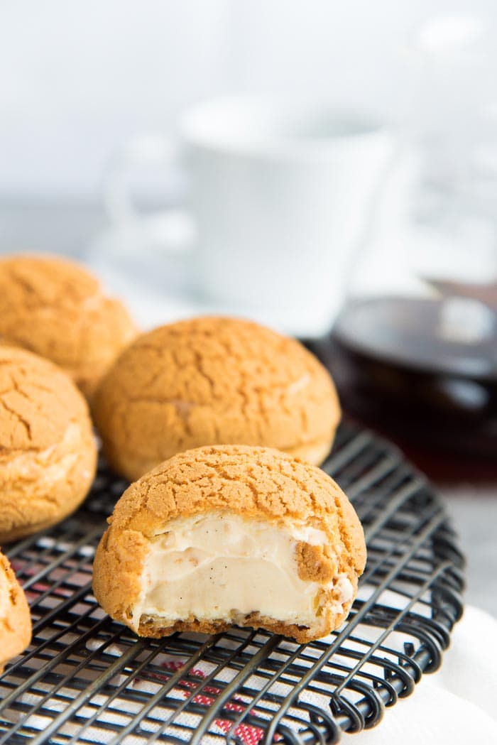 A half eaten salted caramel craquelin choux pastry bun on a black wire rack, with uneaten pastries next to it in the background.
