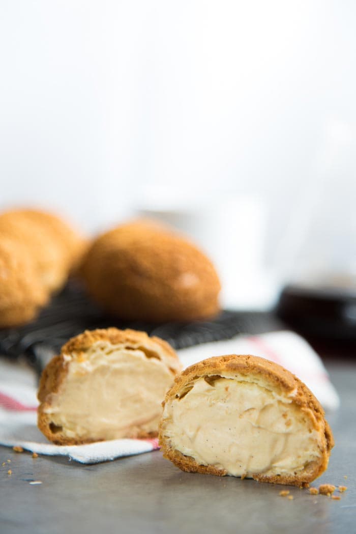 A salted caramel diplomat cream filled choux au craquelin cut in hald in the foreground, with more pastries in the background.