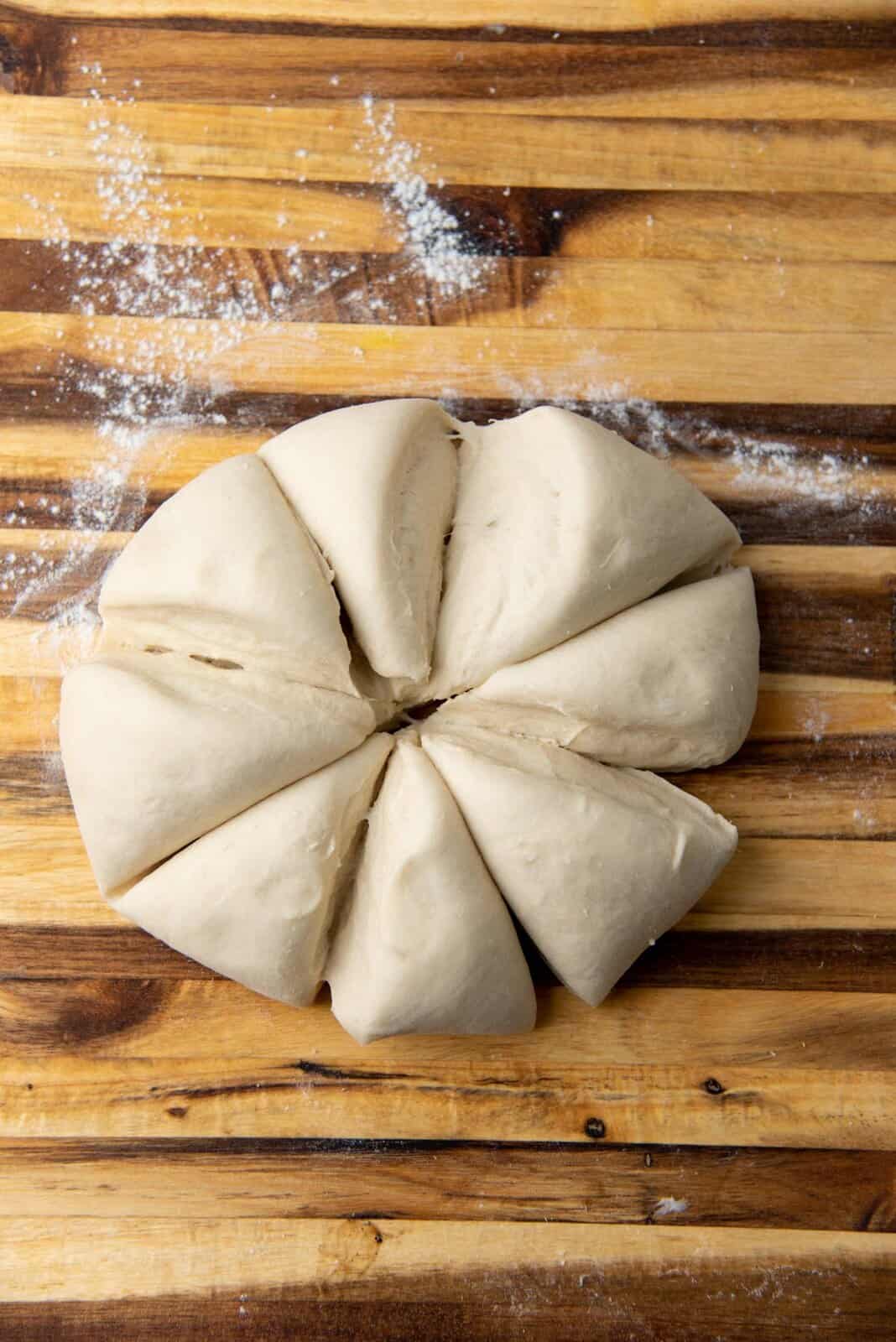 A round dough cut into 8 pieces on a wooden board.