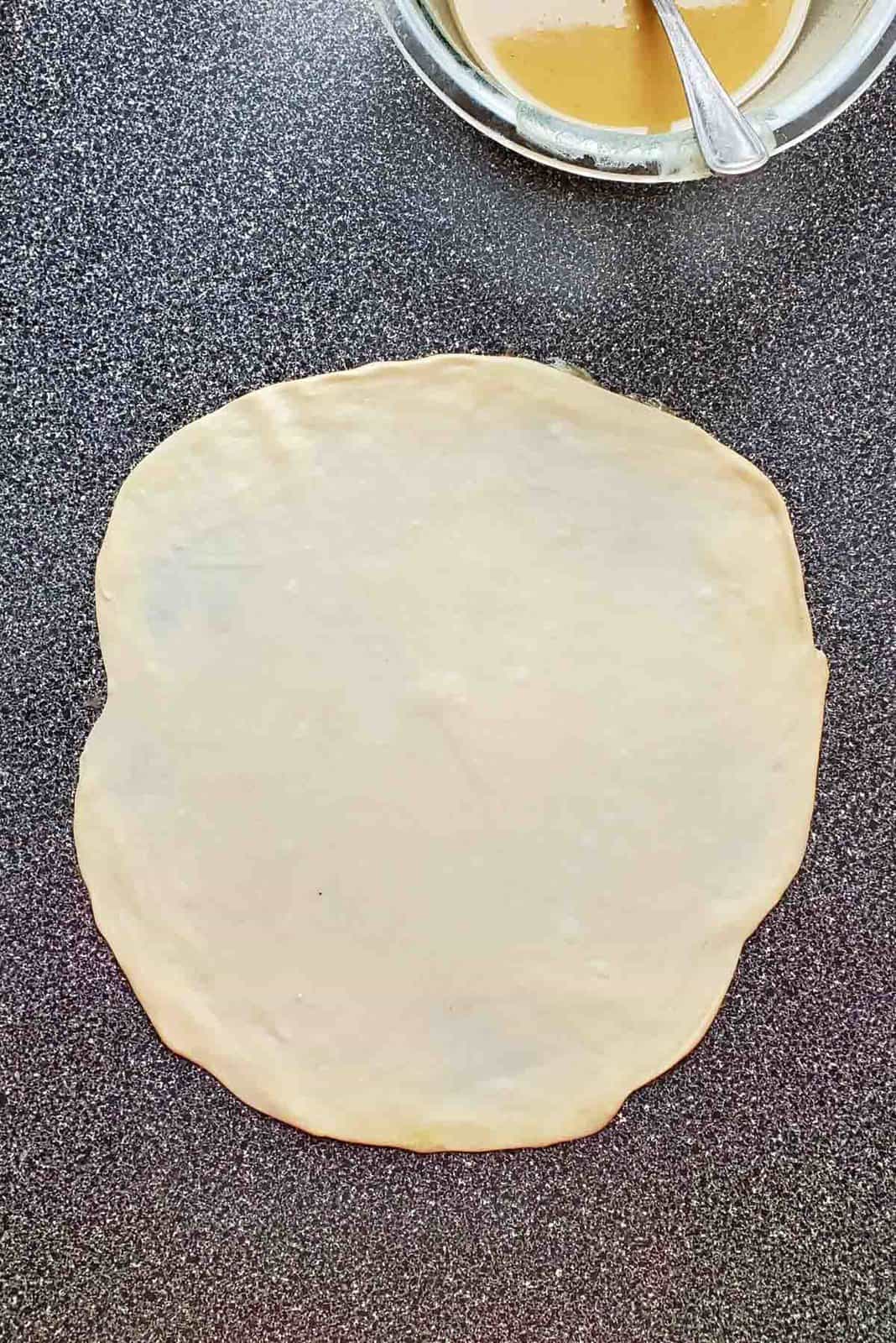 An overhead view of the dough rolled out to a roughly shaped circle.