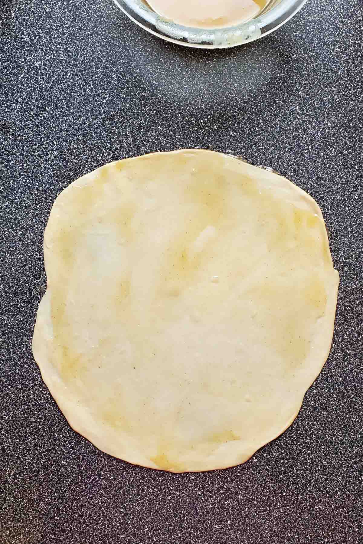 An overhead view of the oil paste spread on the rolled out dough.
