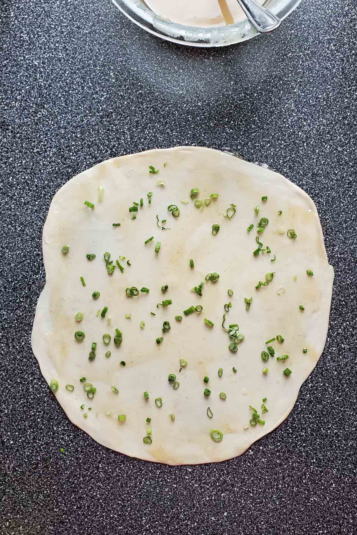 Scallions sprinkled on the surface of the rolled dough.