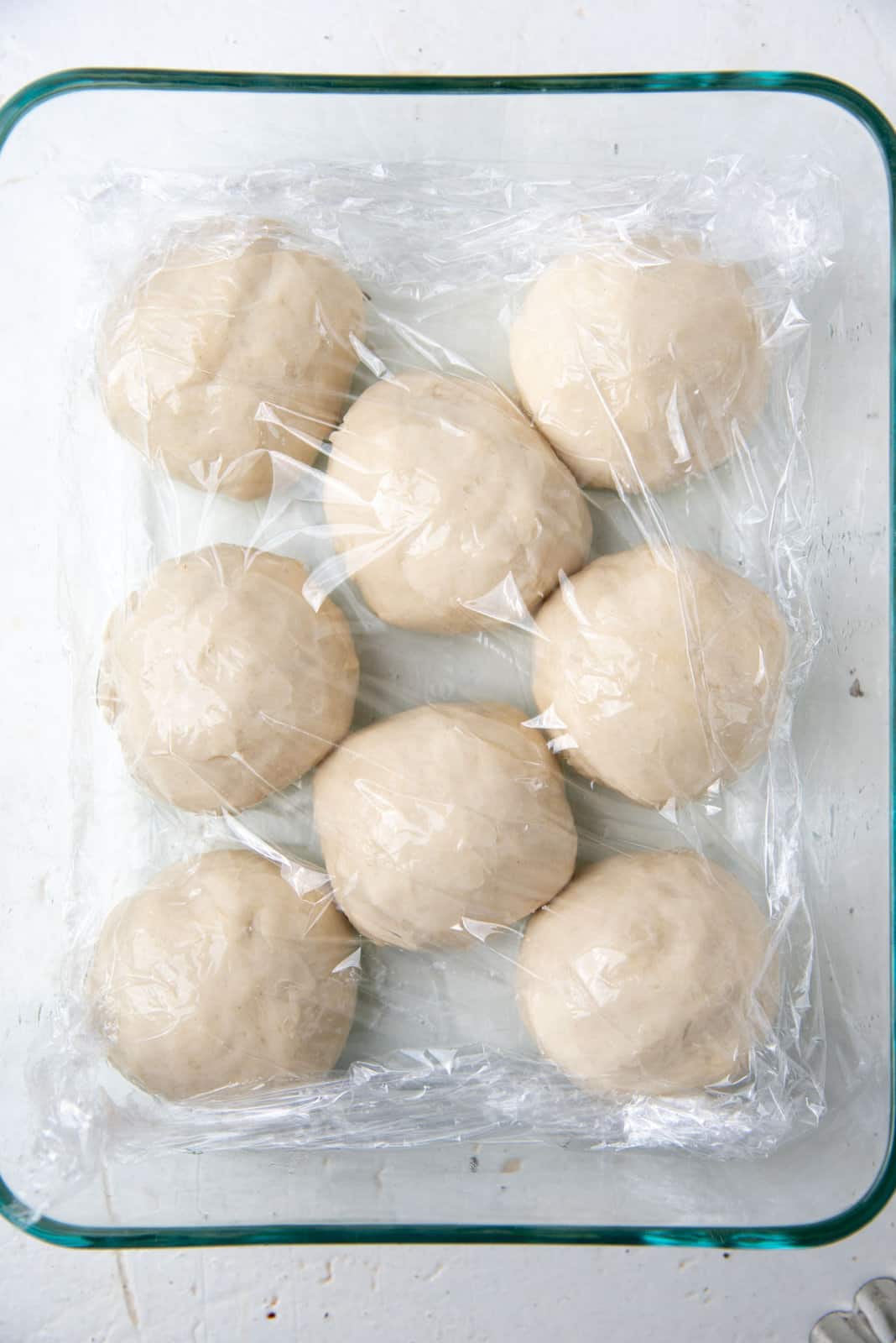 The eight dough ball portions place in a container with oil and covered with plastic wrap.