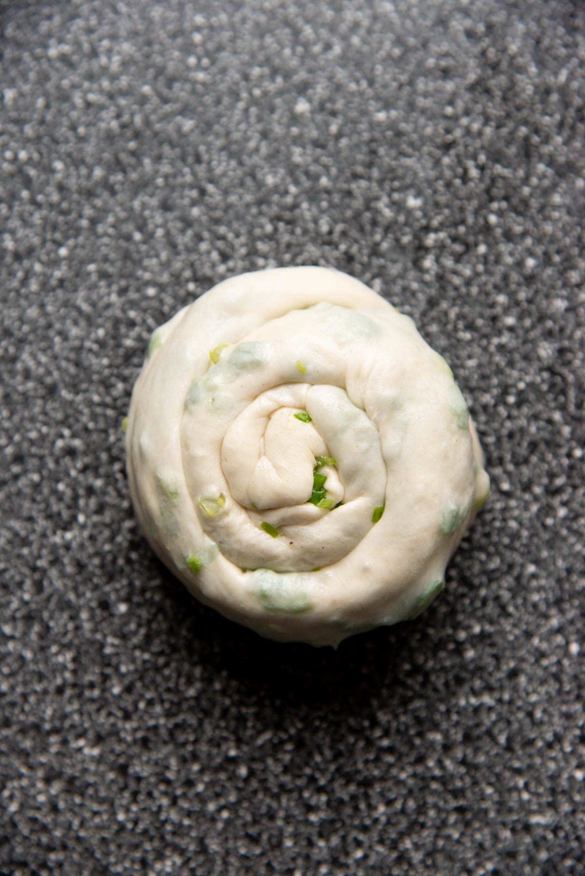A coiled scallion dough portion on a speckled surface.