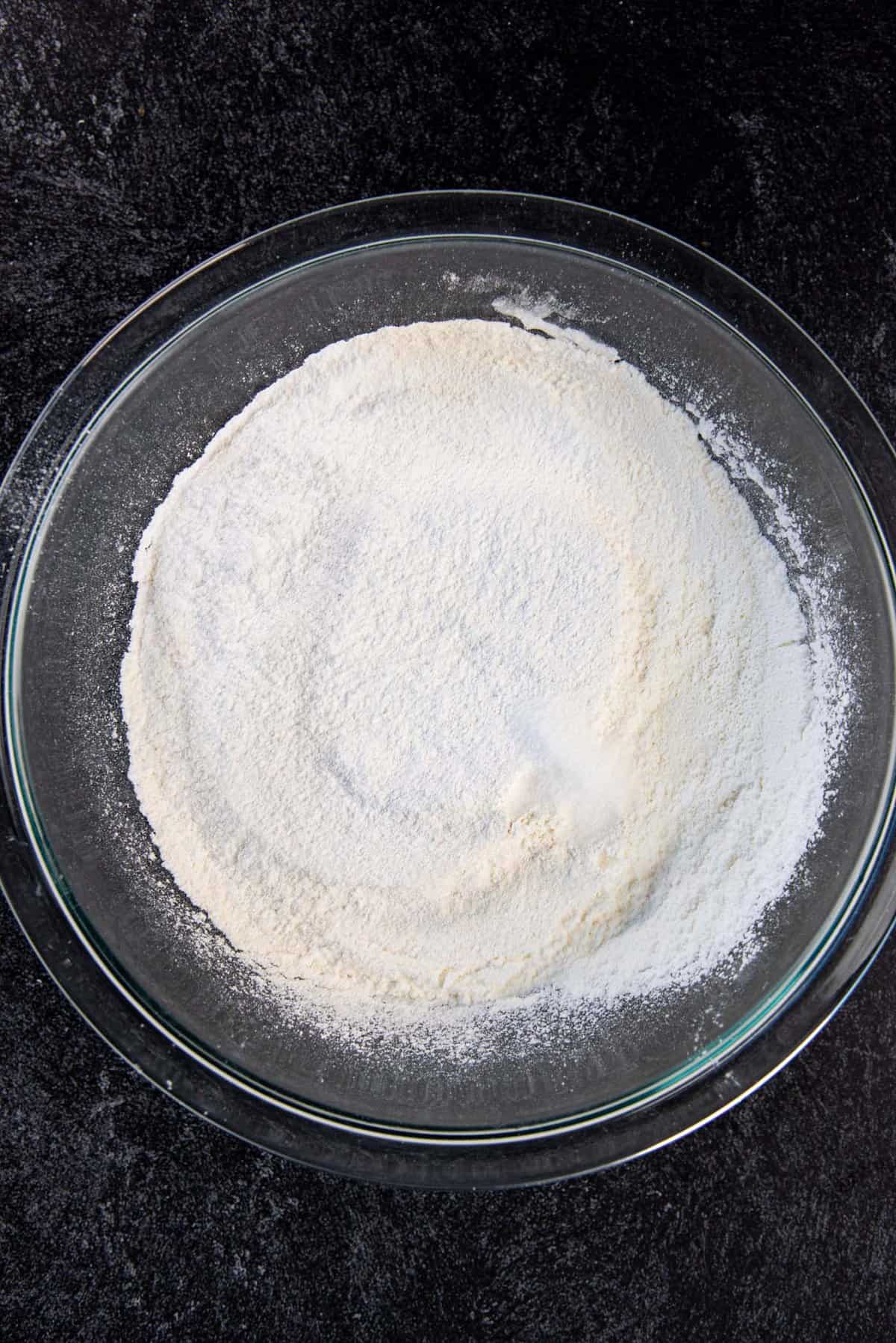 Dry ingredients sifted into a glass bowl, with salt added on top.