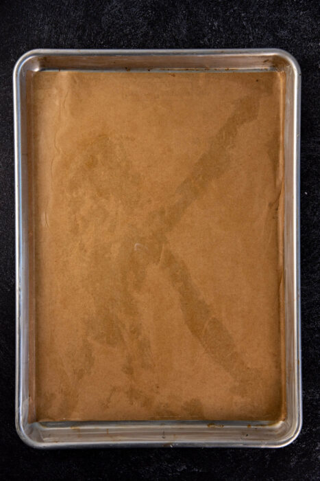 A half sheet pan lined with parchment paper and prepared for the pancake batter.