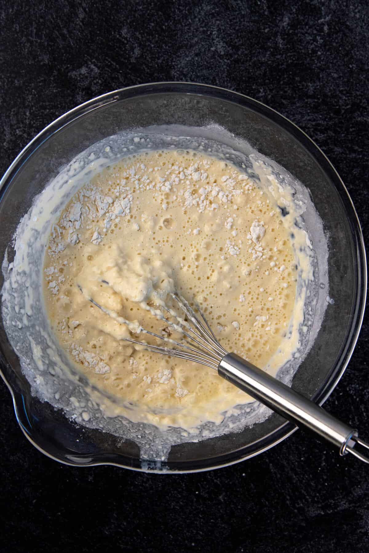 Wet inredients added to the dry ingredients and being gently mixed with a whisk.