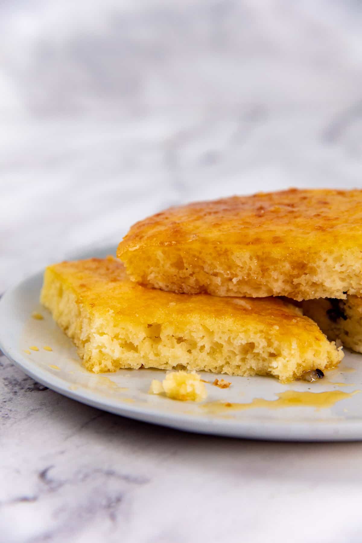 A close up of the oven baked sheet pan pancakes after being reheated, and served on a plate with maple syrup.