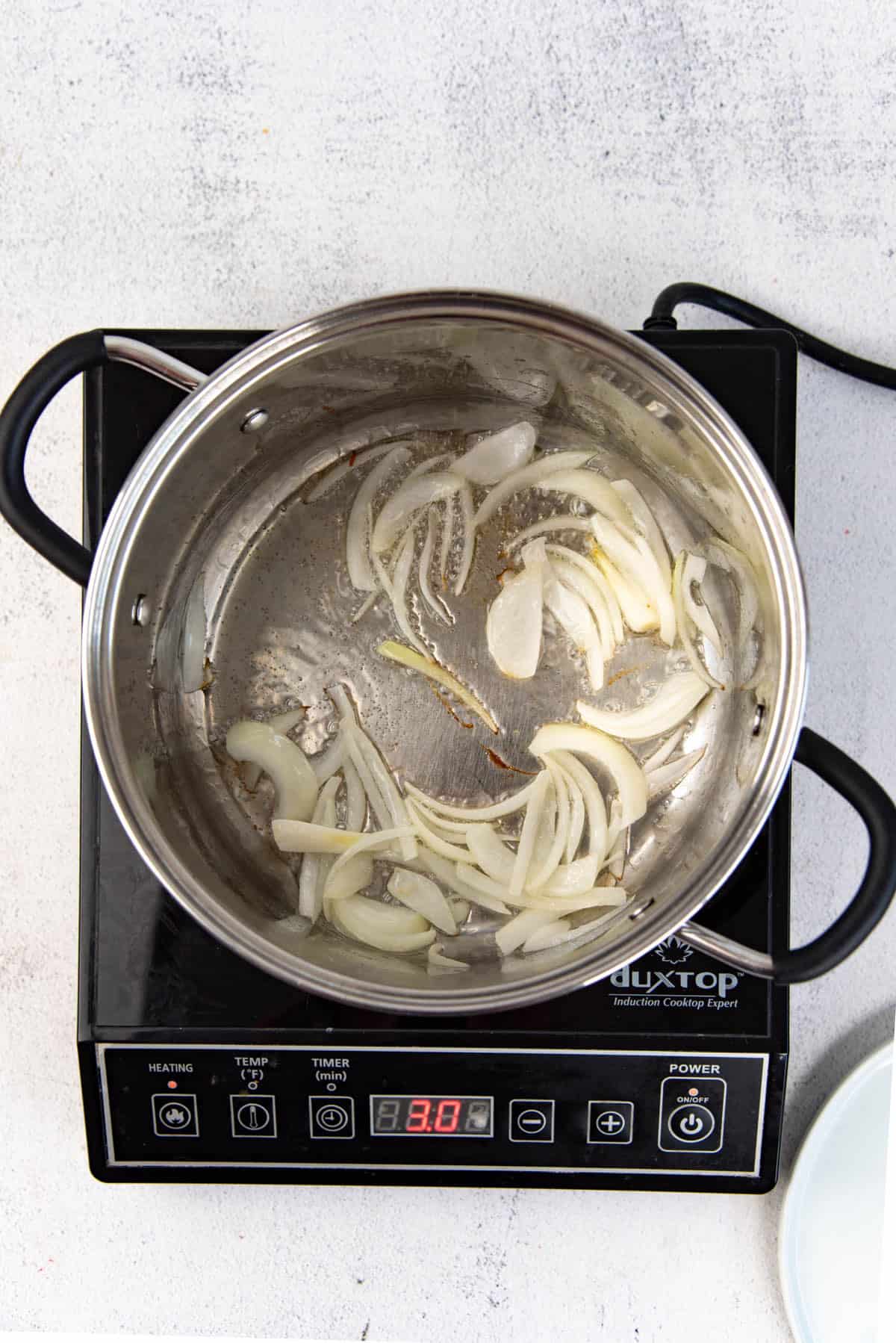 Onions softening in hot oil in stainless steel pot.