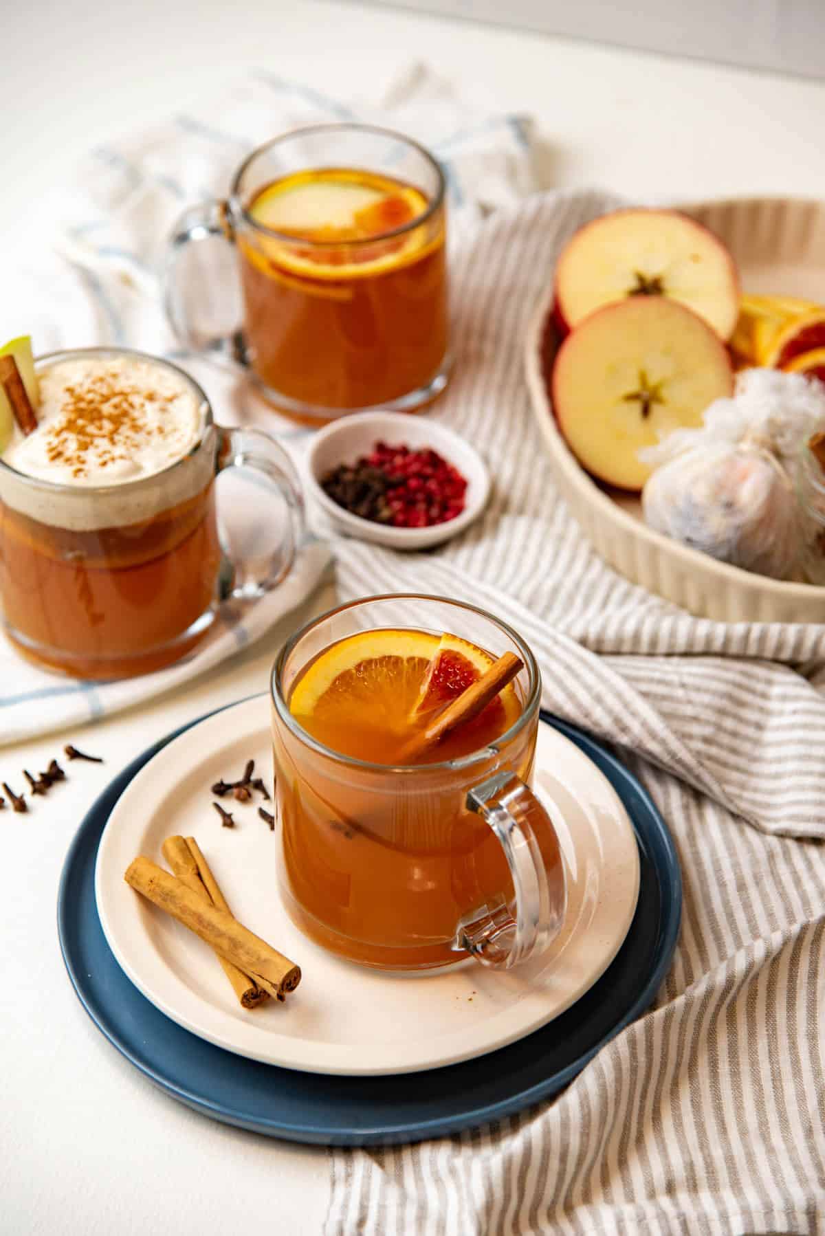 3 glass mugs of mulled apple cider on a white tabletop.