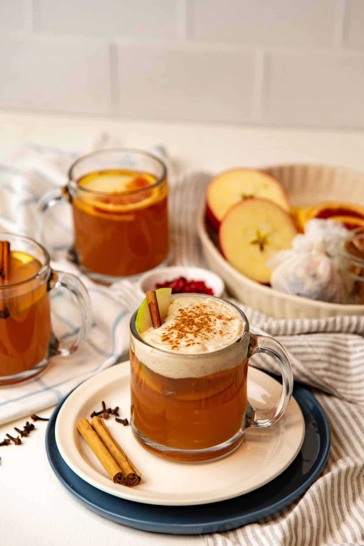 Whipped cream topped apple cider served with garnishes.