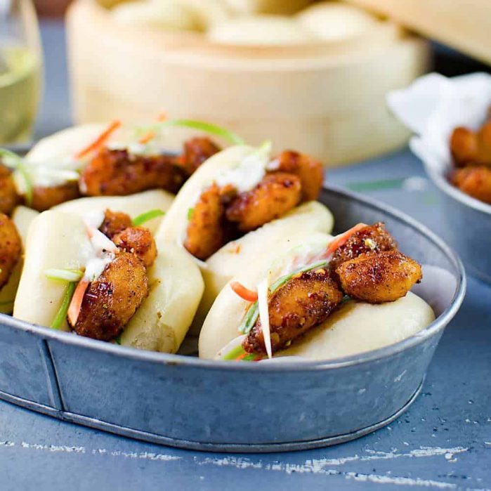 Deliciously easy, Spicy Asian Popcorn Shrimp Bao - Perfect for busy weeknights. Restaurant-quality, flavor-packed meal in just 15 - 20 minutes with crispy oven-baked popcorn shrimp, tossed in a spicy Asian sauce and then served with steamed Chinese bao buns (or slider buns) with crunchy carrots and spring onions!  