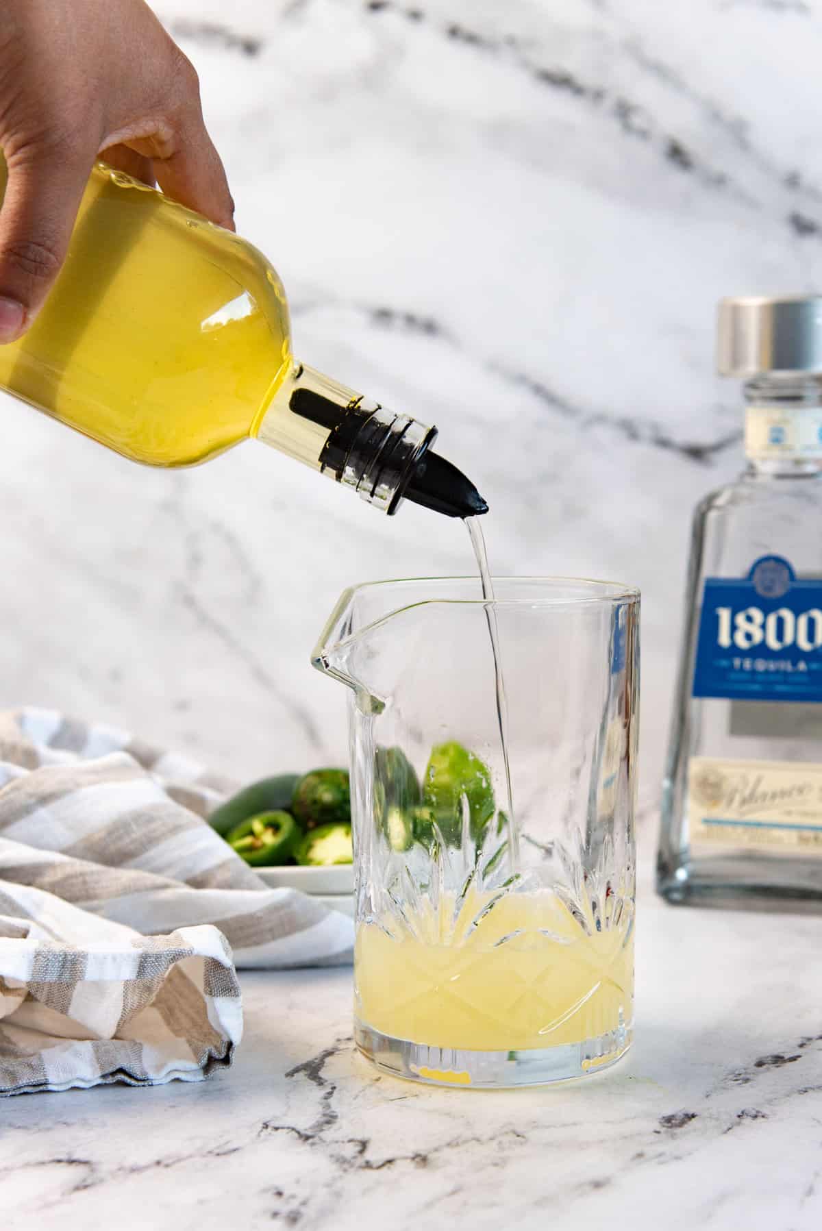 Pouring jalapeno simple syrup into a cocktail mixer.