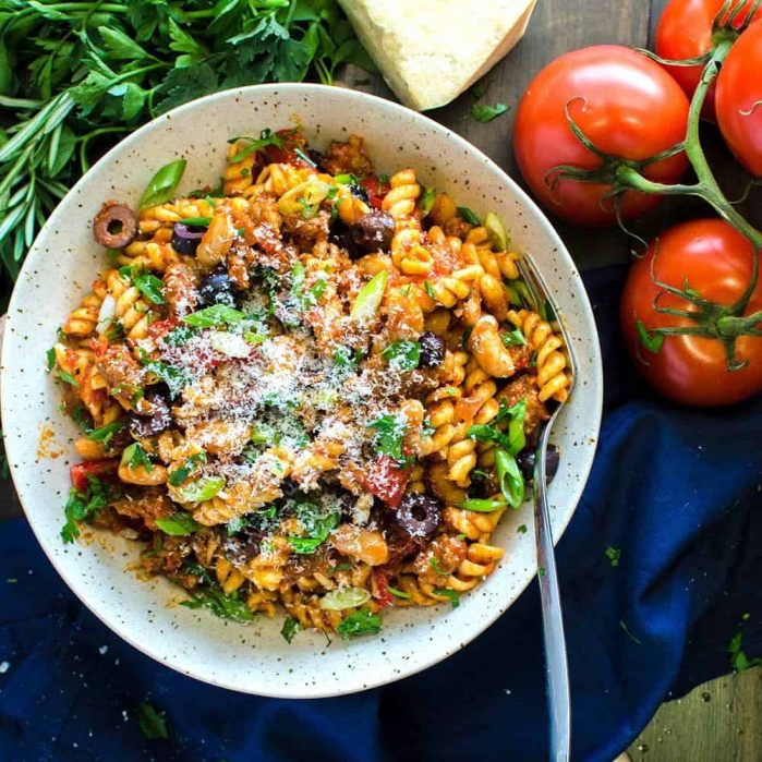Bowl of spicy Tuscan sausage pasta served with cannellini beans, olives, grated cheese etc. on top.