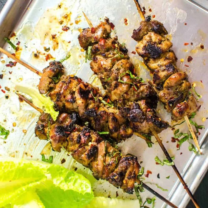 Four spicy Thai chicken skewers on a sheet pan with some romaine lettuce leaves next to them.
