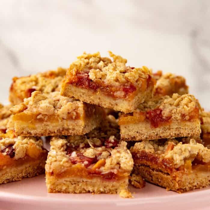 Stack of baked peach bars with crumble topping on a pink plate.