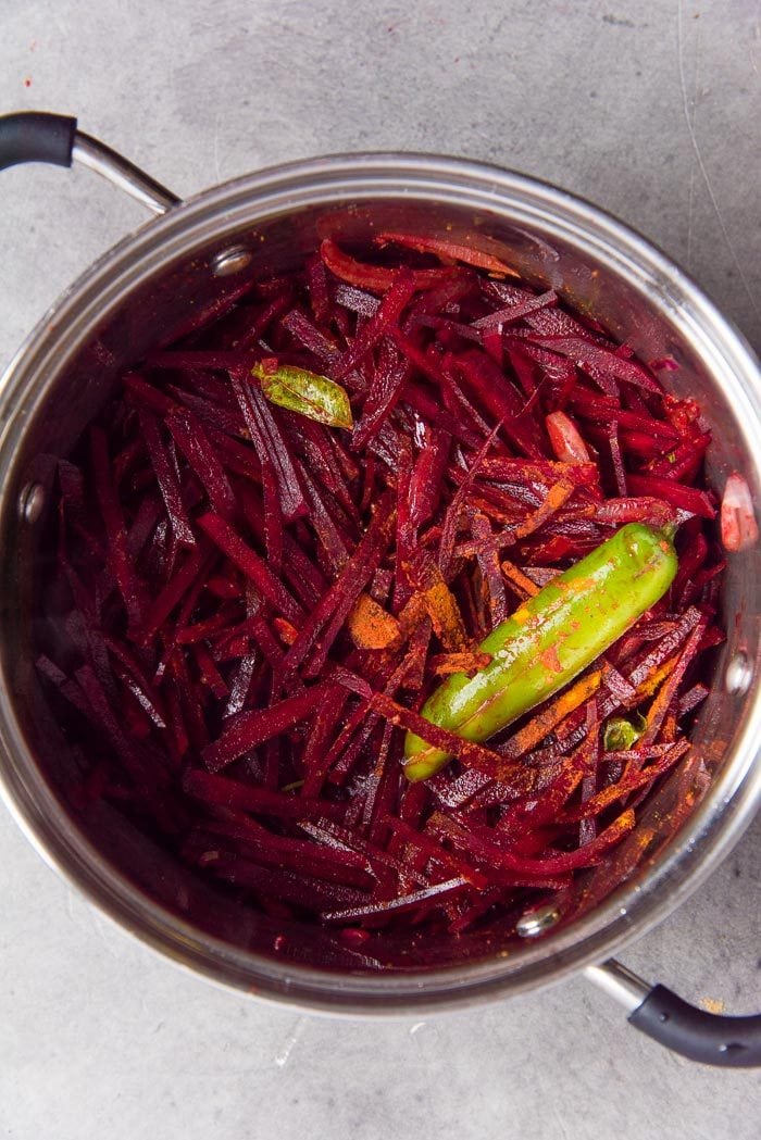 Ingredients for a beetroot curry placed in a saucepan, with curry leaves, green chili.
