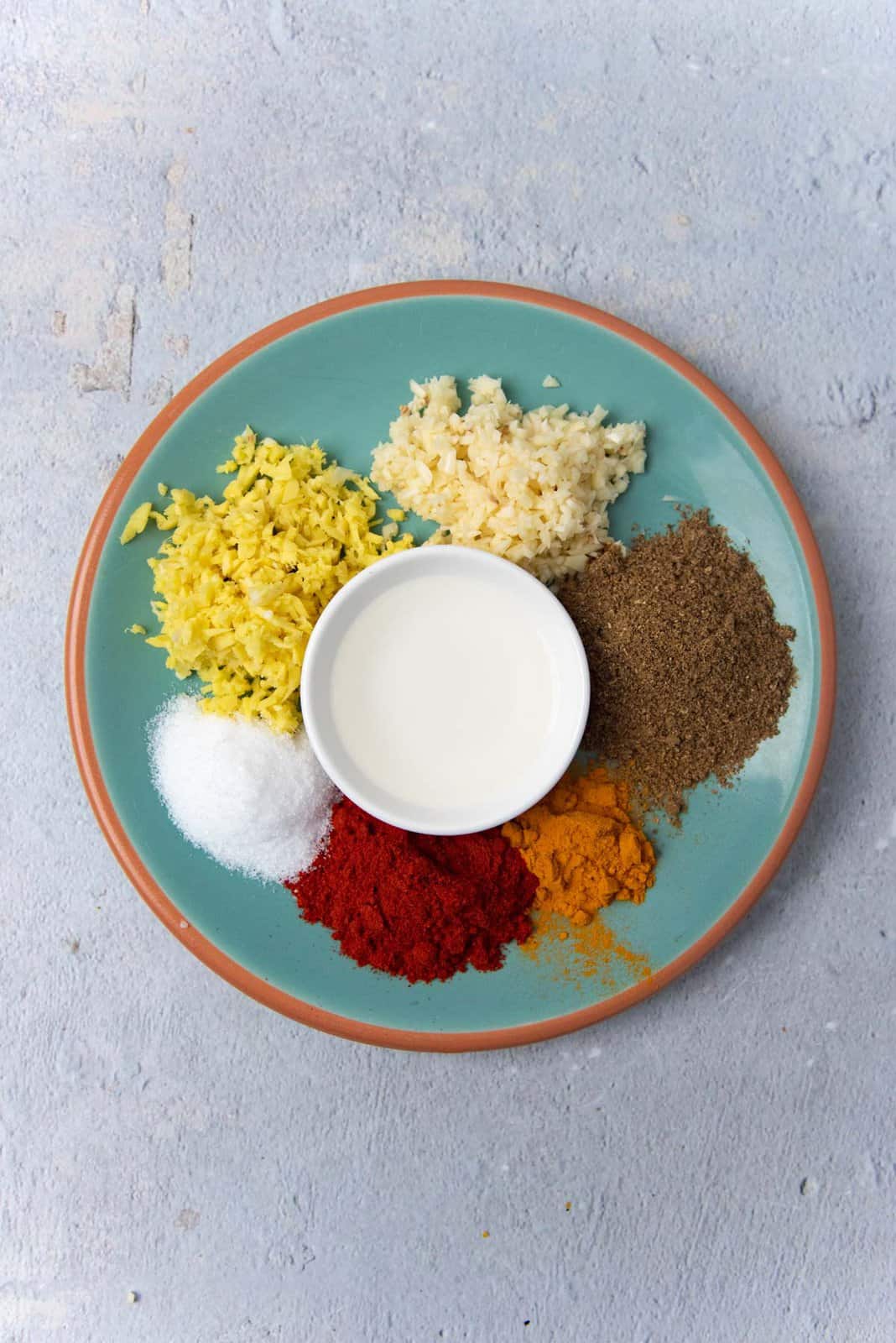 A green plate, with different mounds of spices and aromatics placed, as the marinade ingredients for the mutton.