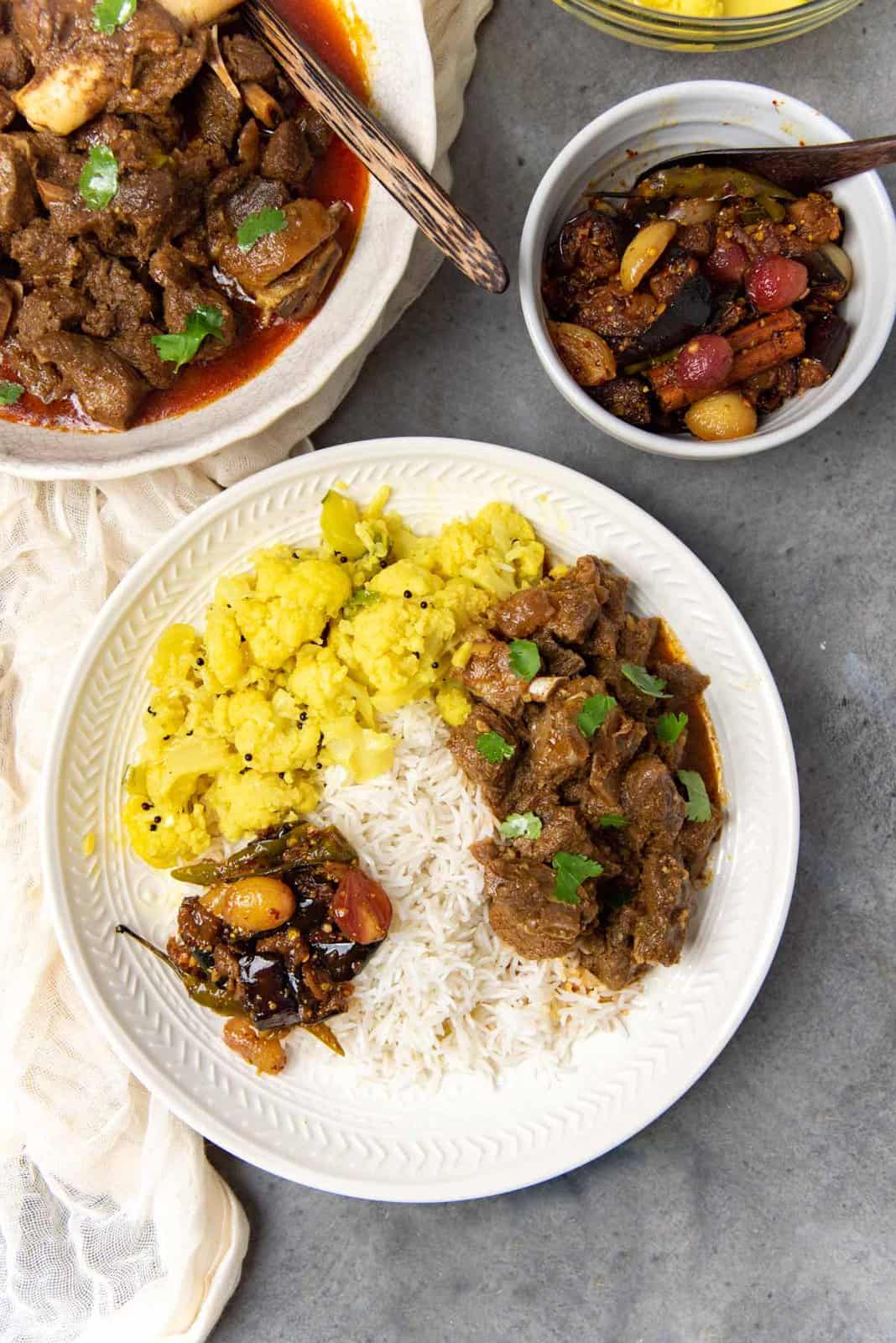 An overhead view of the lamb curry served on a bed of rice with other vegetable side dishes.