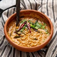 Red lentil curry (parippu curry) in a big clay pot with a wooden serving spoon.