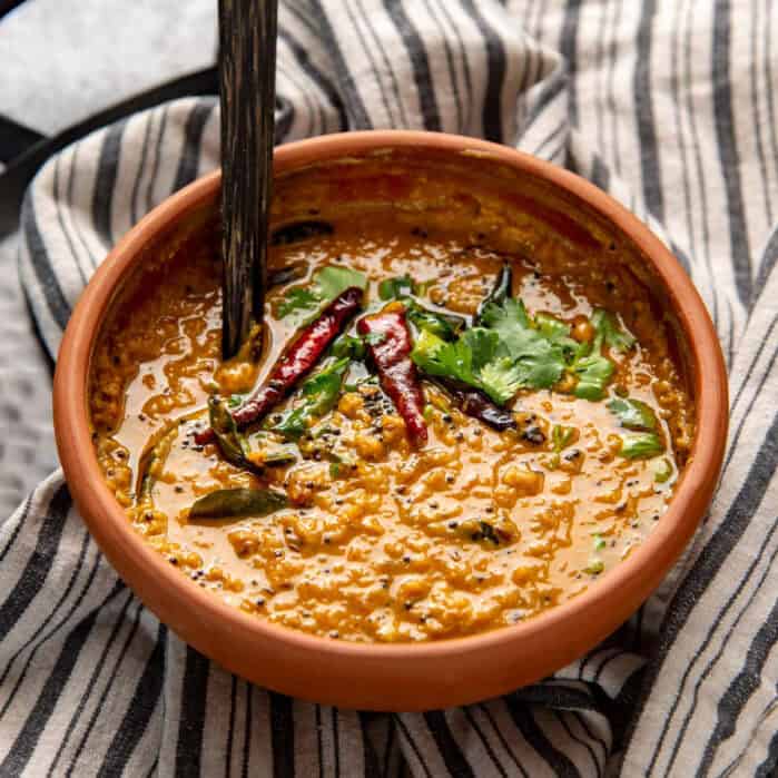 Red lentil curry (parippu curry) in a big clay pot with a wooden serving spoon.