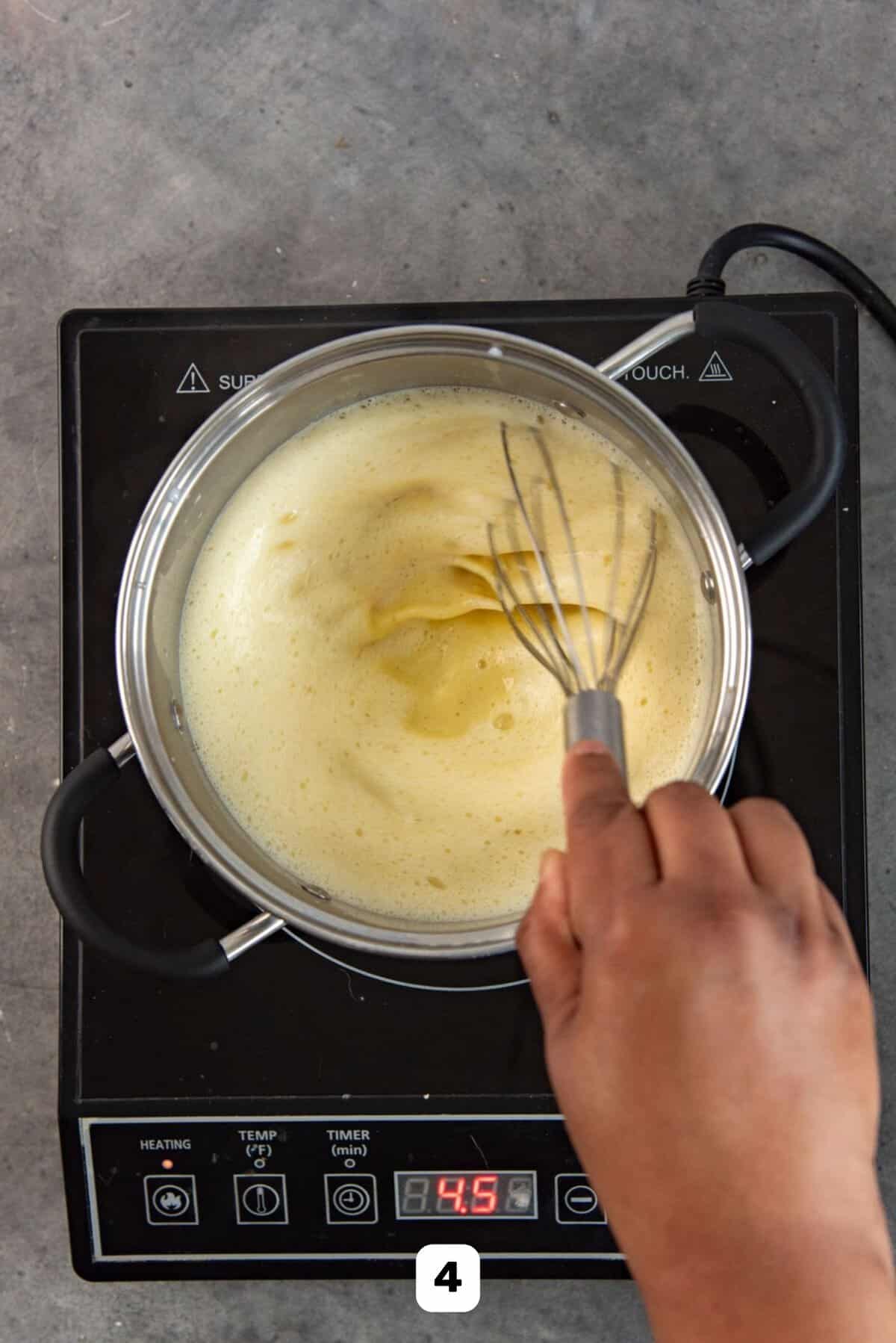Stirring pastry cream mixture with whisk, while cooking it on a stove to thicken.