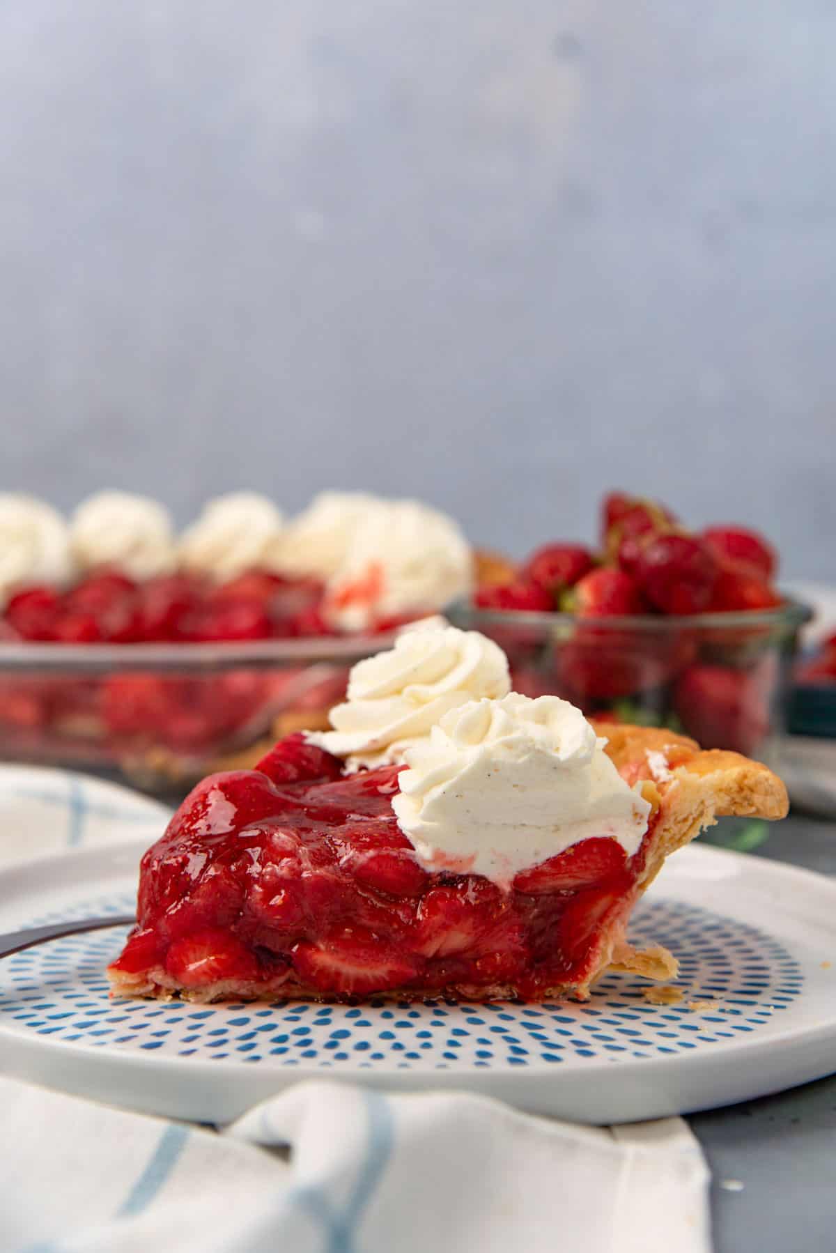 Fresh strawberry pie slice on a white and blue plate with whipped cream on top.