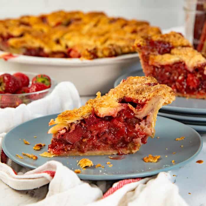 Strawberry rhubarb pie slice on a plate and rest of the pie in the background.