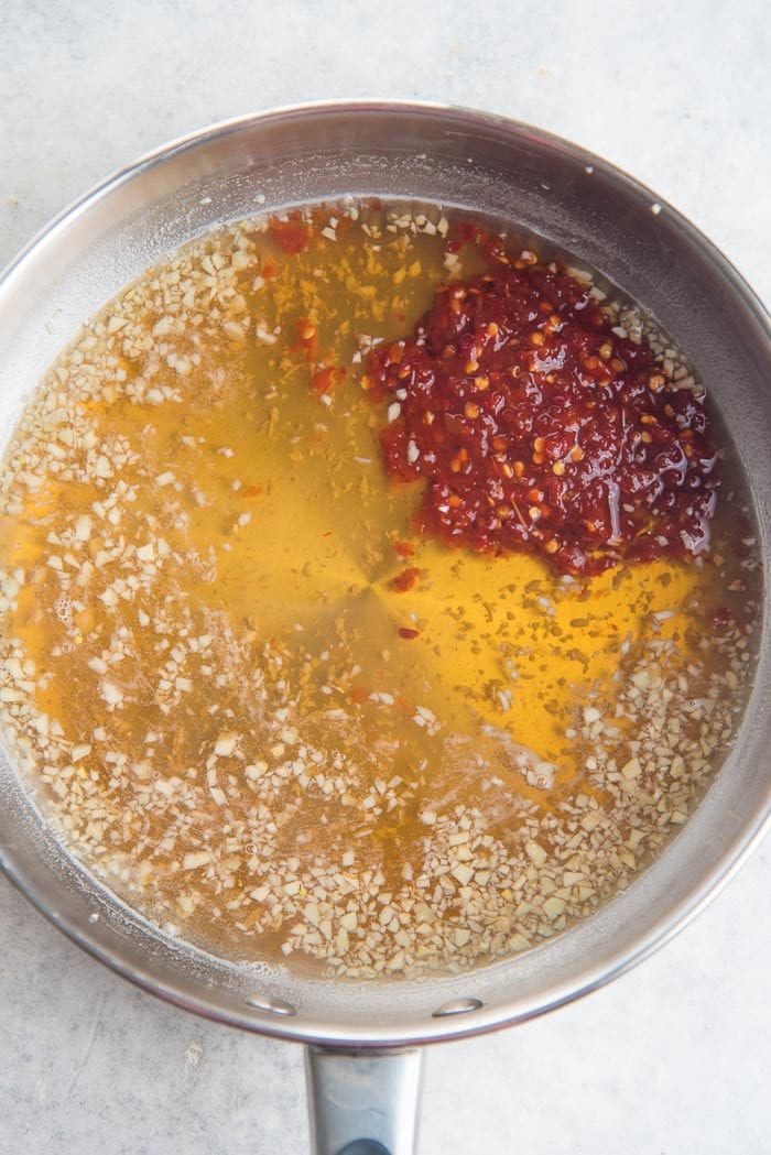 Sambal oelek being added to the saucepan once the sugar has melted in the liquid - overhead view