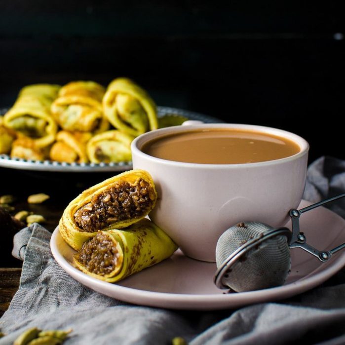 A pani pol cut in half to show the sweet coconut filling inside, next to a cup of tea.